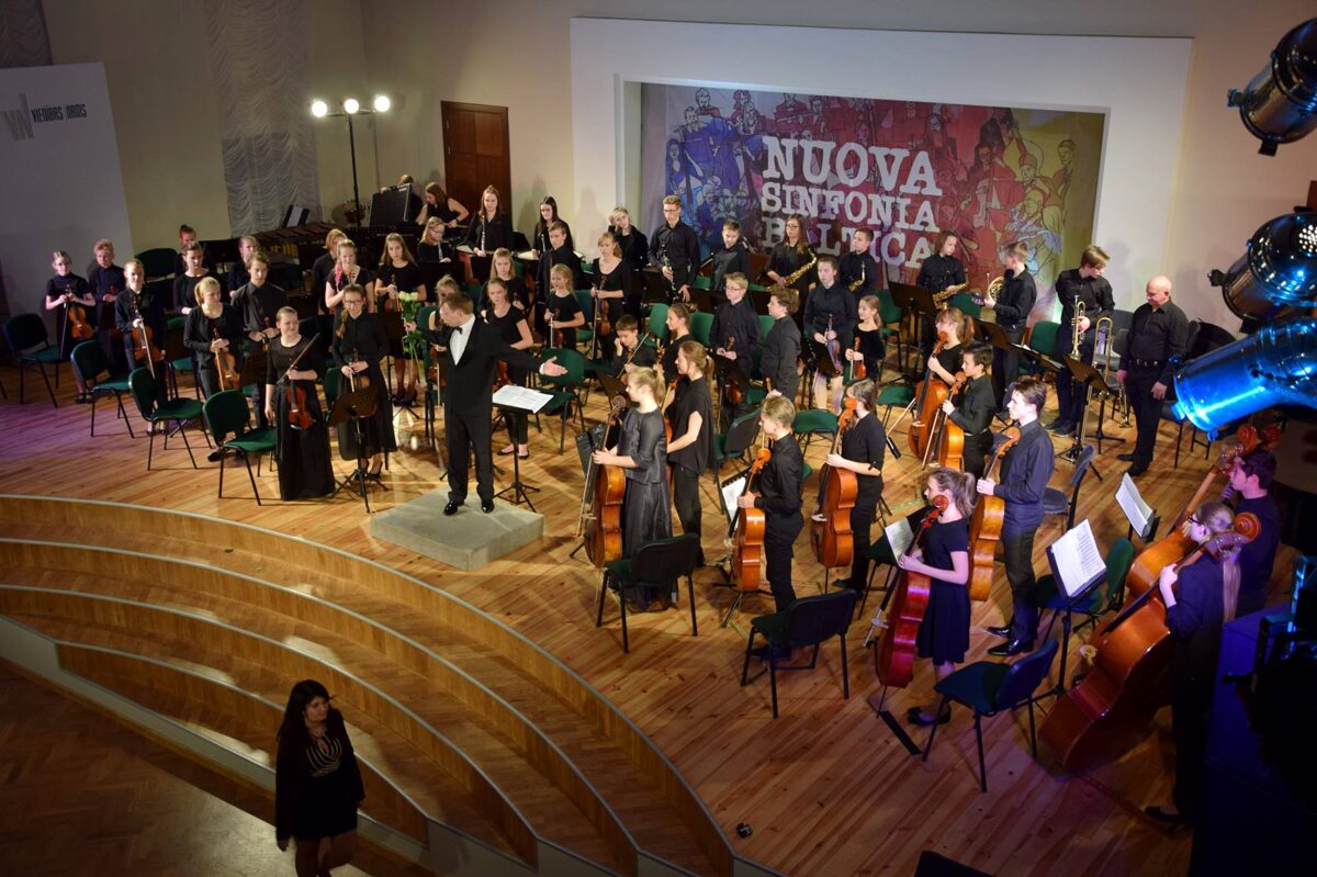 Juglas Mūzikas skolas šimfoniskais orķestris uz skatuves ar diriģentu Mārci Miķelsonu, skats no augšas